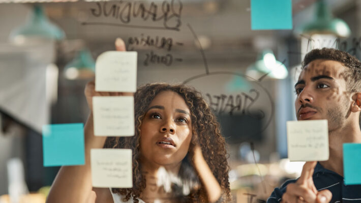 a man and woman looking at sticky notes on a glass board