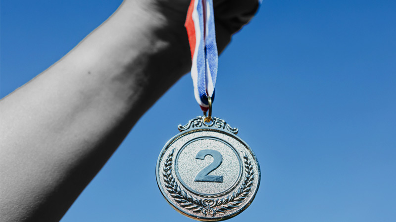 a gray hand holding a silver medal with the number two on it
