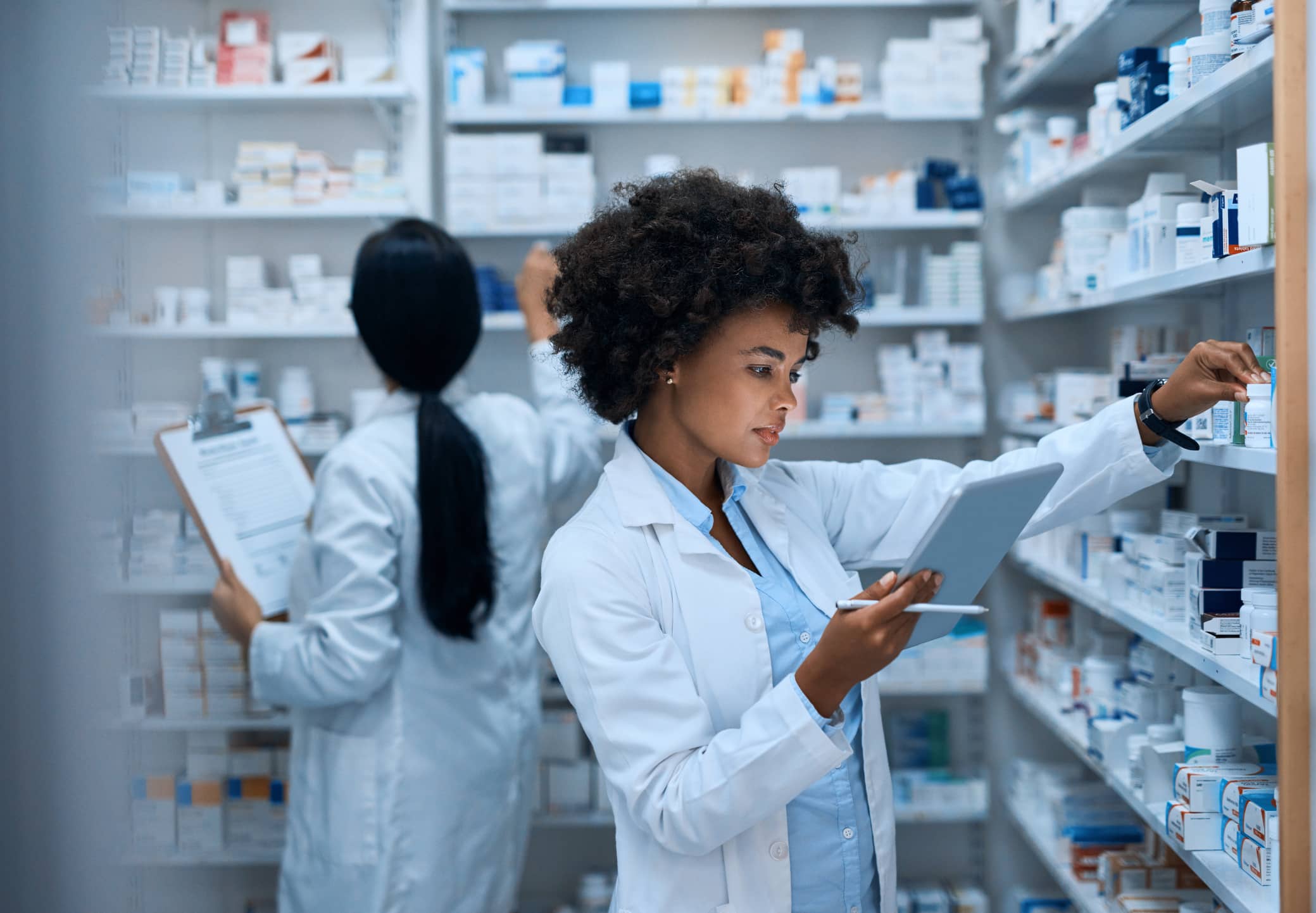 Two pharmacists selecting medications and subscriptions from shelves of pharmaceutical products