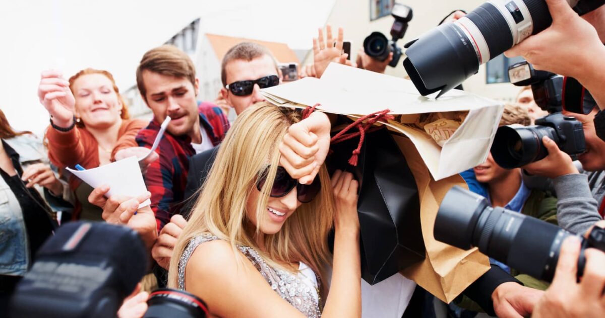 A blonde celebrity with sunglasses pushing through fans and paparazzi