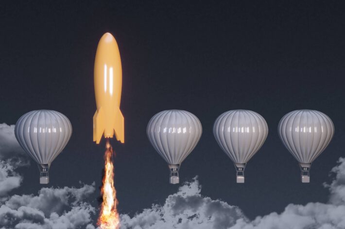 Four gray balloons and one golden rocket with exhaust beneath it