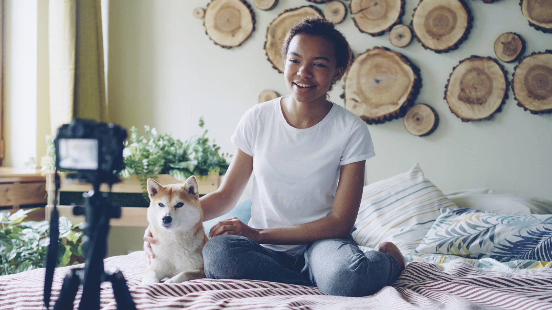 a woman filming a video of her self talking to the camera while sitting on the bed with her dog