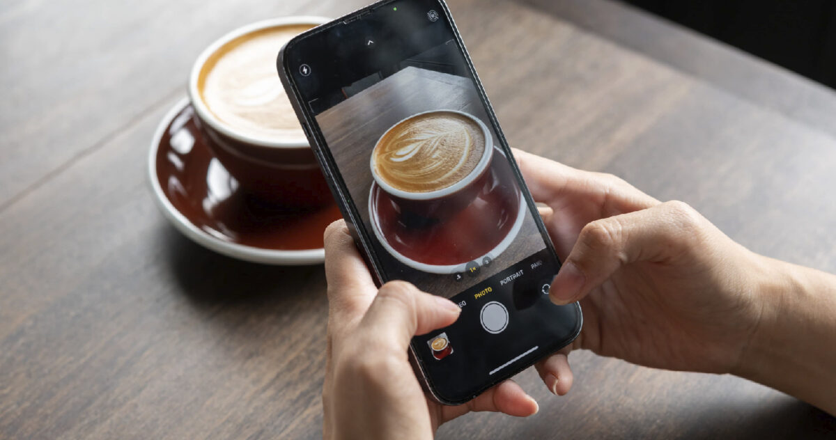 hands holding a phone taking a photo of a cappuccino 