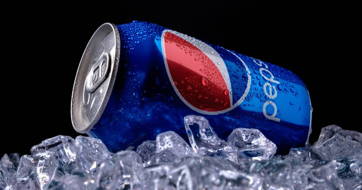 Black background, melting ice on the bottom of the image with a Pepsi can on top of the ice laying on its side with condensation on the can