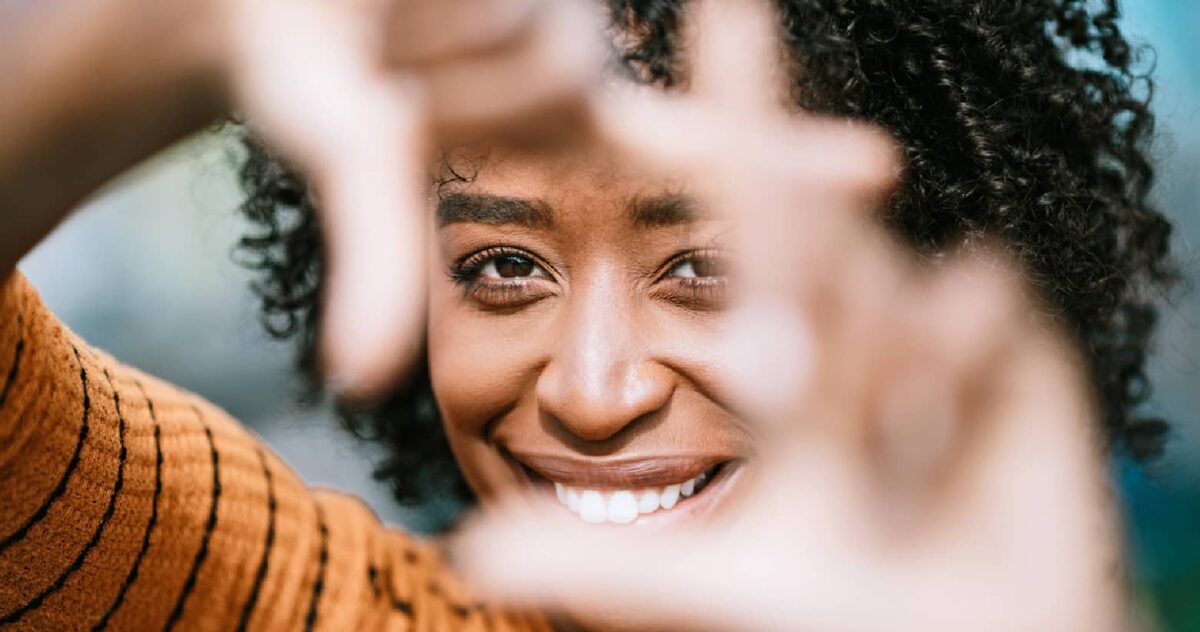 A woman's face framed by her hands as if on a camera screen