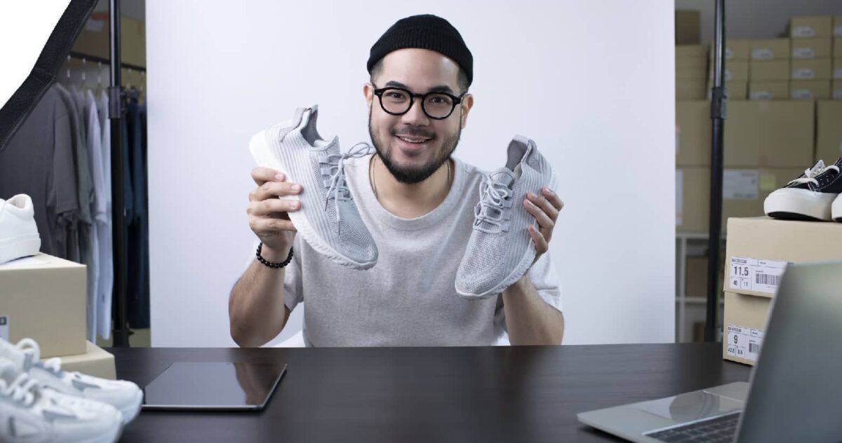 man in a skull cap with glasses holding up a pair of white tennis shoes 