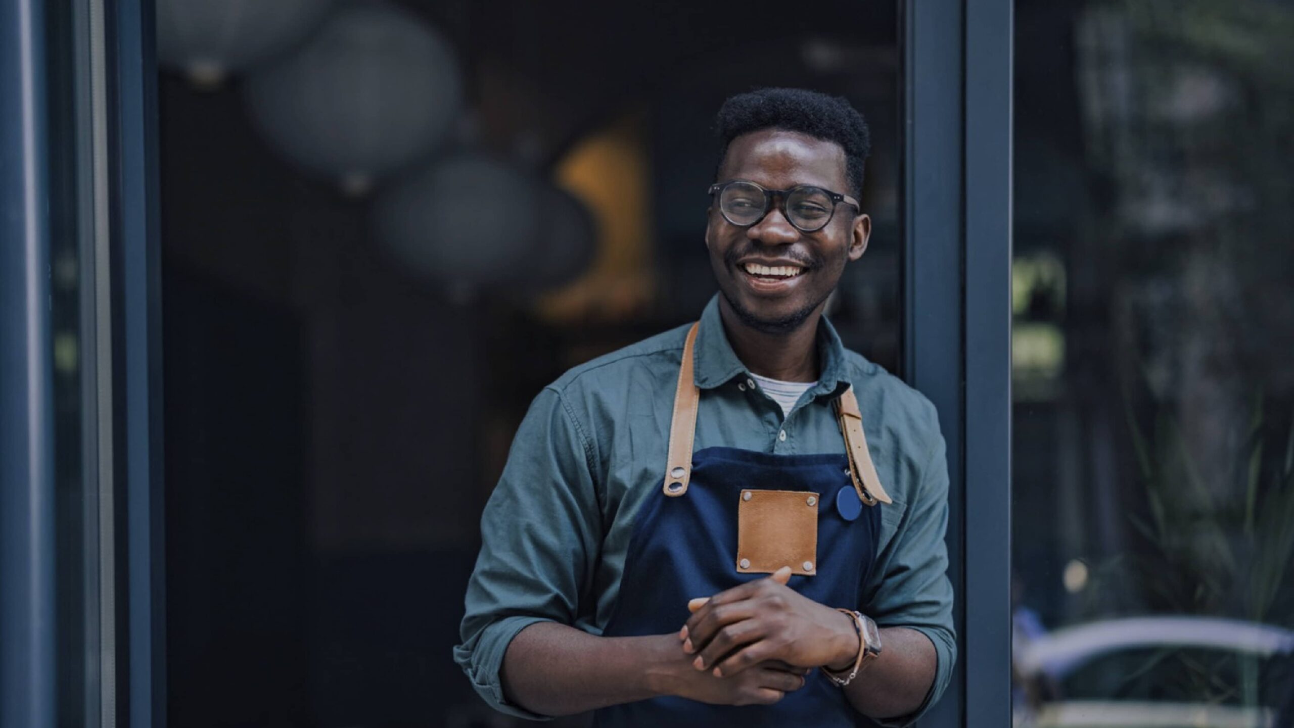 A young Black man in an apron smiling in the doorway