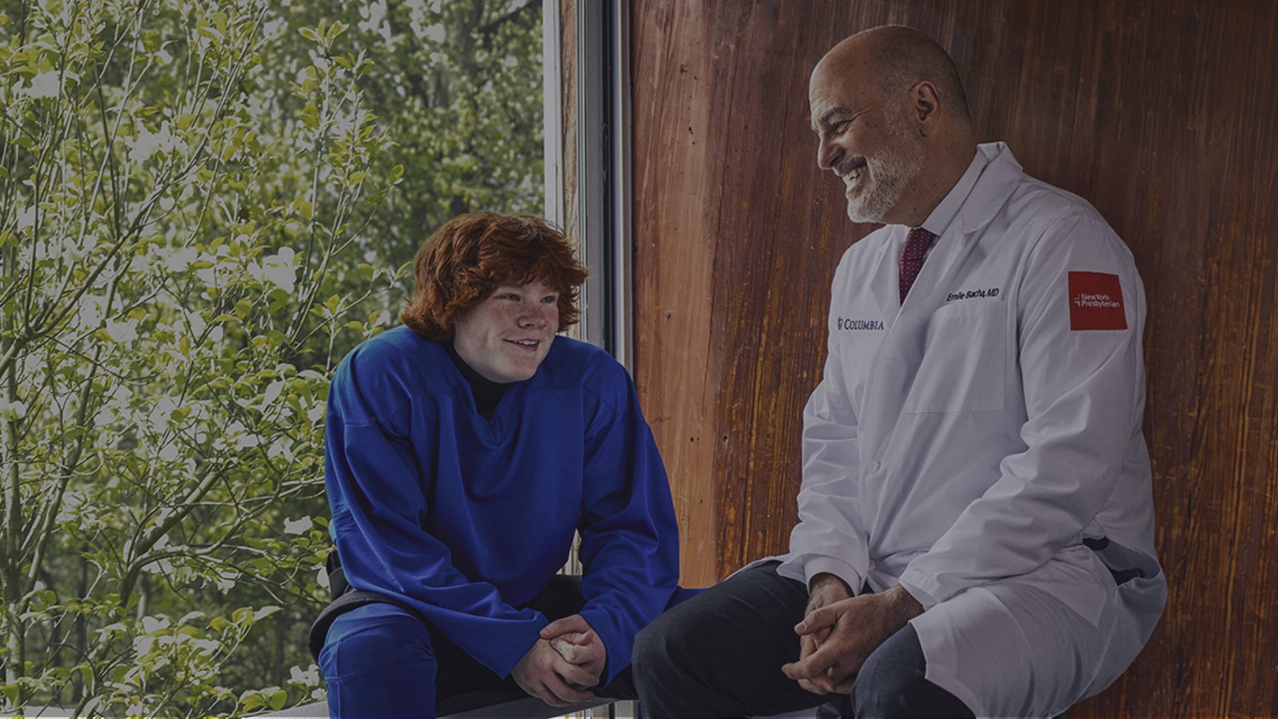 A NewYork Presybterian physician sits with a young man by a window