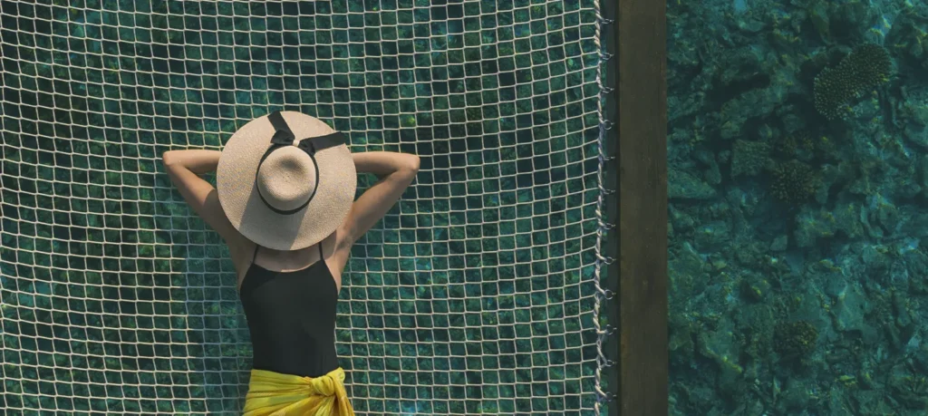 A woman relaxing on a suspended net above the sea, part of journey-based thinking in travel.