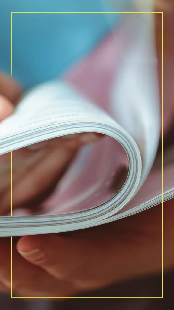 Person turning pages in a printed magazine, illustrating engagement with print media.
